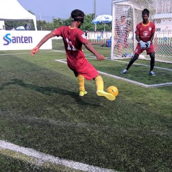 A blind player strikes the ball from outside the goalkeepers box towards the goal of the sighted keeper